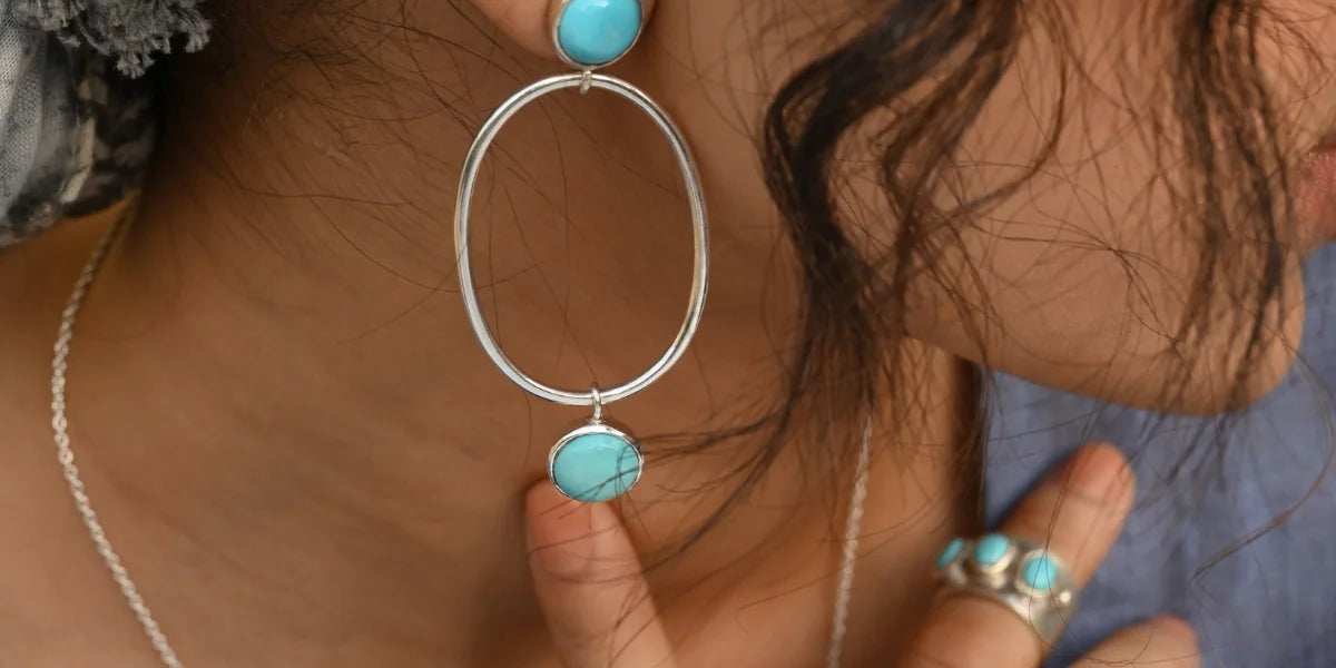 Turquoise gemstone drop earrings worn by a woman